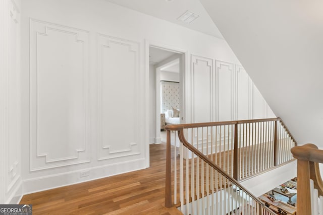 hall with an upstairs landing, a decorative wall, light wood finished floors, and visible vents