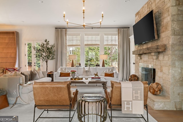 living area with a chandelier, a stone fireplace, and light wood-style flooring