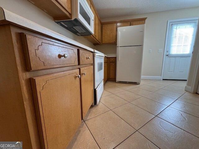 kitchen with brown cabinetry, baseboards, freestanding refrigerator, light tile patterned flooring, and a textured ceiling