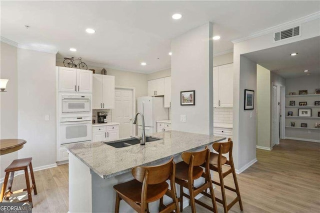 kitchen with a breakfast bar area, ornamental molding, white appliances, white cabinetry, and a sink