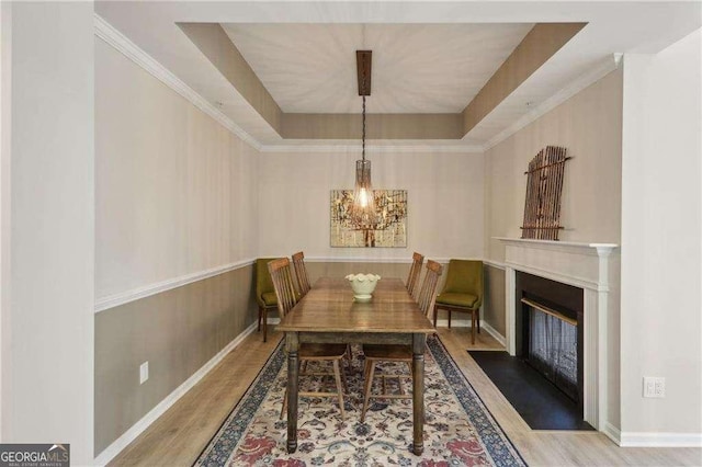 dining area featuring an inviting chandelier, a tray ceiling, a fireplace with flush hearth, and wood finished floors