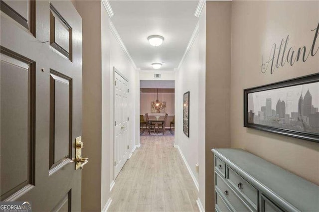 hallway featuring light wood finished floors, visible vents, crown molding, and baseboards