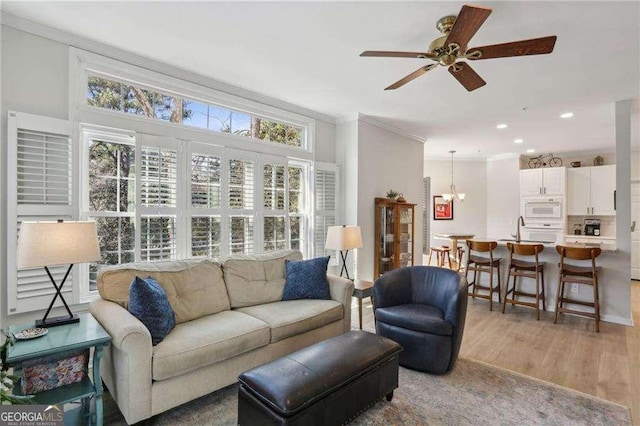 living room featuring recessed lighting, light wood-style floors, crown molding, and ceiling fan with notable chandelier