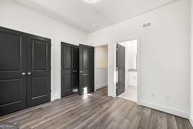 unfurnished bedroom featuring visible vents, baseboards, two closets, and wood finished floors
