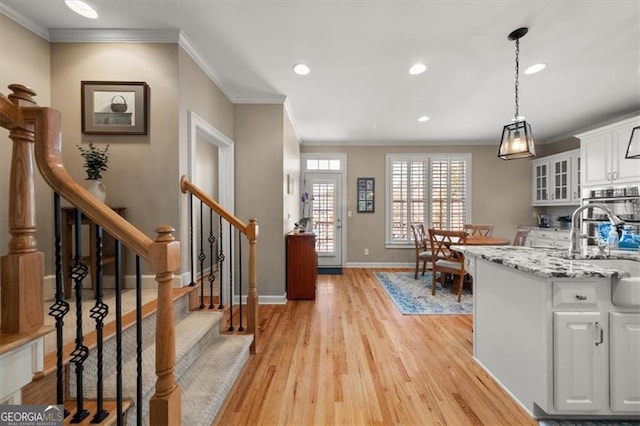 kitchen featuring glass insert cabinets, baseboards, crown molding, light wood-style flooring, and white cabinets