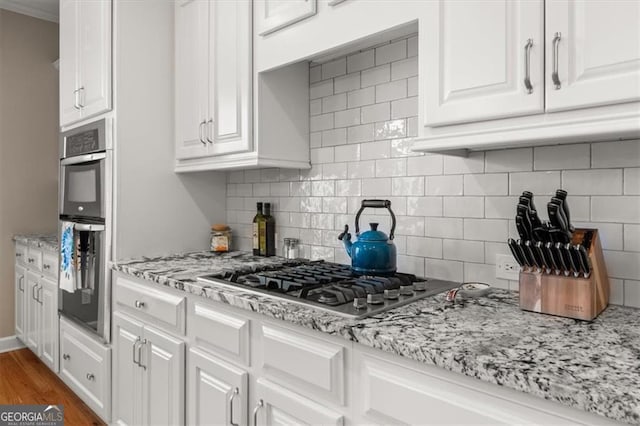 kitchen featuring decorative backsplash, appliances with stainless steel finishes, white cabinetry, and wood finished floors