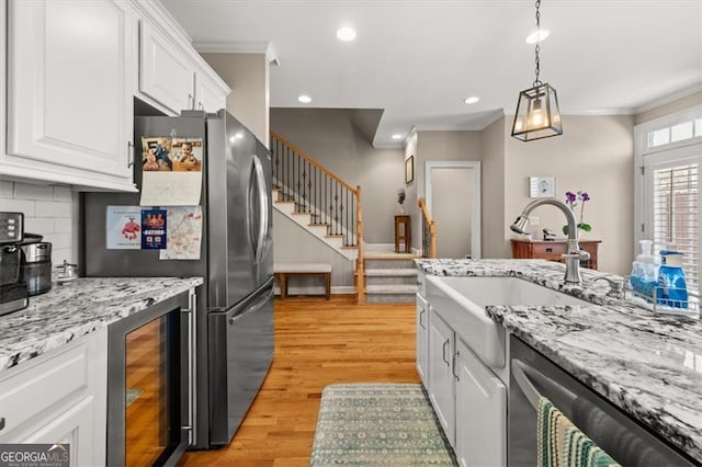 kitchen featuring beverage cooler, a sink, light wood-style floors, white cabinets, and crown molding