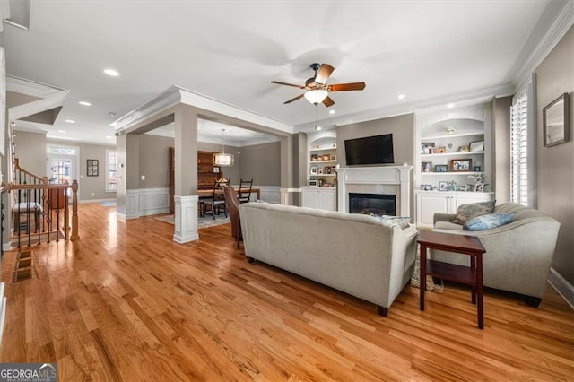 living area with light wood-type flooring, built in shelves, crown molding, and stairway