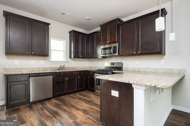 kitchen featuring dark brown cabinetry, dark wood-style flooring, appliances with stainless steel finishes, a peninsula, and a sink