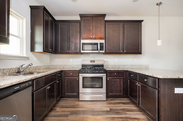 kitchen featuring a peninsula, a sink, dark brown cabinetry, dark wood-type flooring, and appliances with stainless steel finishes