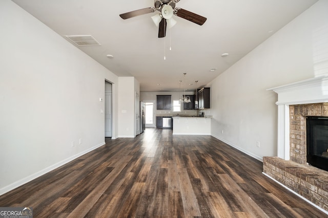 unfurnished living room featuring visible vents, a brick fireplace, baseboards, dark wood finished floors, and a ceiling fan