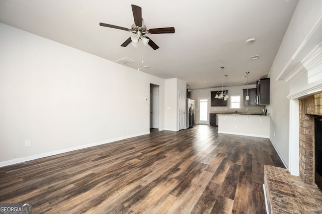 unfurnished living room featuring visible vents, baseboards, ceiling fan with notable chandelier, a fireplace, and dark wood-style floors