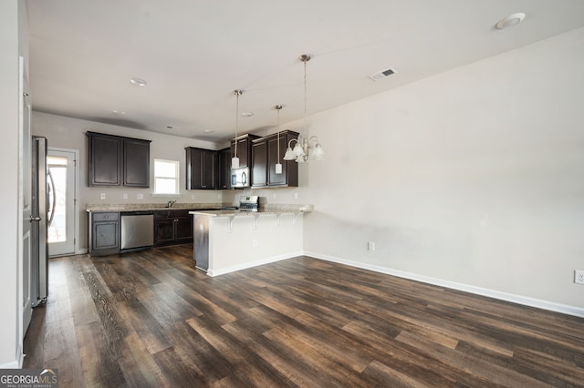 kitchen featuring visible vents, a peninsula, dark brown cabinetry, dark wood-type flooring, and appliances with stainless steel finishes