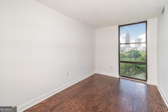 empty room with visible vents, baseboards, dark wood finished floors, a textured ceiling, and a view of city