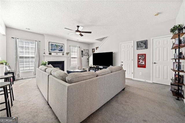 living room featuring a textured ceiling, plenty of natural light, a fireplace, and light carpet