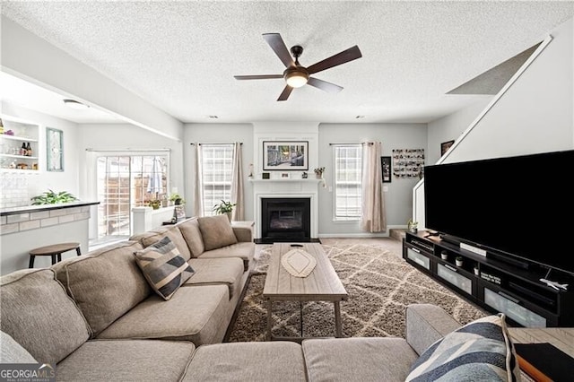 carpeted living room with baseboards, a large fireplace, a textured ceiling, and a ceiling fan