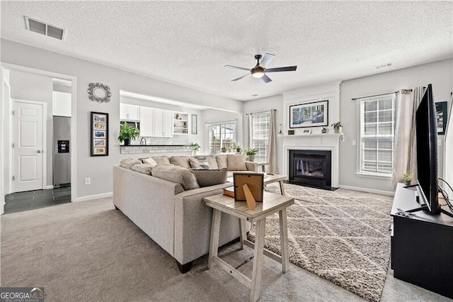 living room featuring visible vents, a fireplace, ceiling fan, a textured ceiling, and light carpet