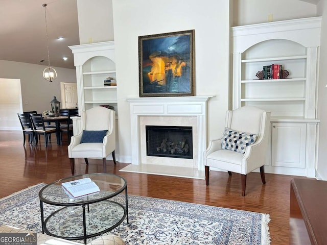 living room featuring built in features, an inviting chandelier, wood finished floors, and a high end fireplace