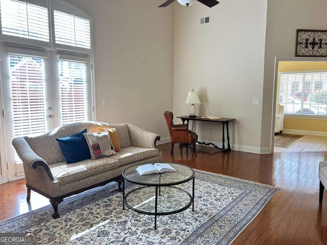 living area featuring visible vents, baseboards, ceiling fan, a towering ceiling, and wood finished floors