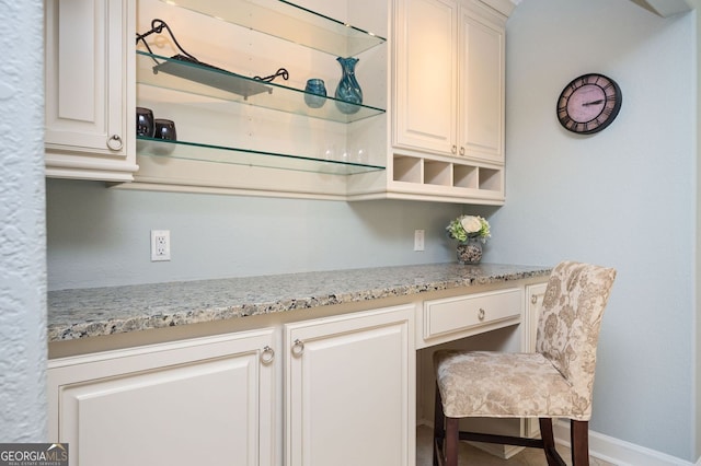 kitchen featuring open shelves, light stone counters, baseboards, and built in desk