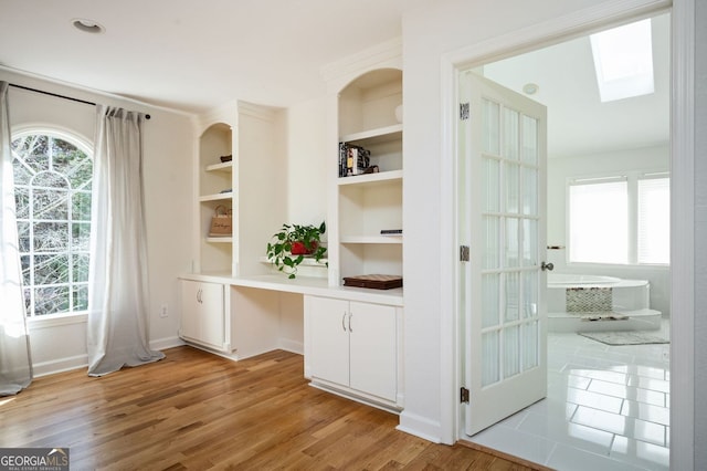 interior space featuring light wood-type flooring, a healthy amount of sunlight, a skylight, and built in desk