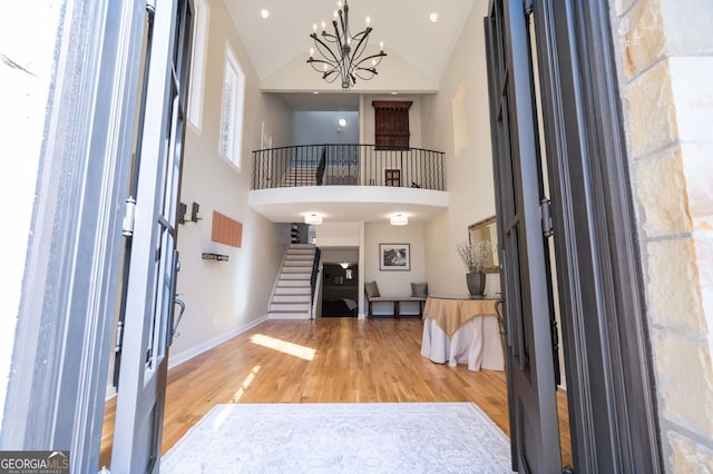 foyer featuring wood finished floors, baseboards, high vaulted ceiling, stairs, and a chandelier