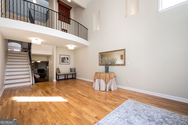 unfurnished room featuring a high ceiling, stairway, wood finished floors, and baseboards