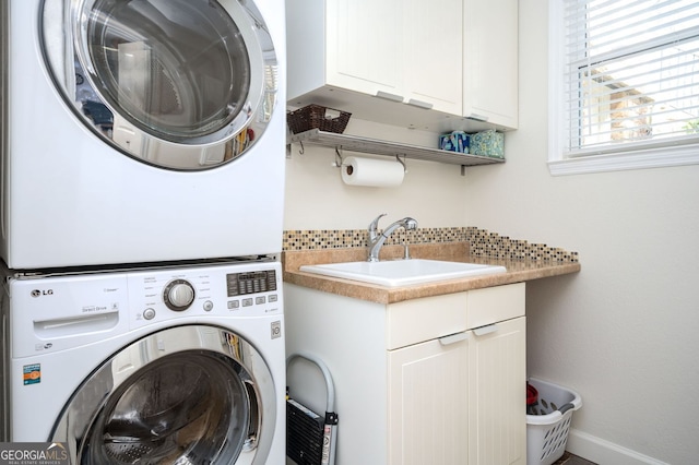 clothes washing area featuring a sink, baseboards, cabinet space, and stacked washing maching and dryer