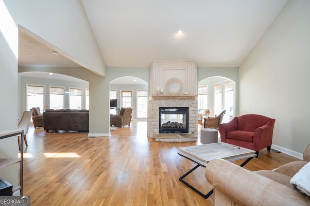 living room featuring baseboards, a multi sided fireplace, light wood finished floors, and high vaulted ceiling