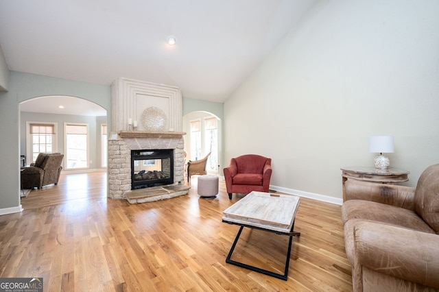 living room with light wood-type flooring, baseboards, arched walkways, and a fireplace