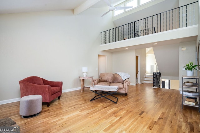 living area with an upstairs landing, beam ceiling, a ceiling fan, wood finished floors, and baseboards