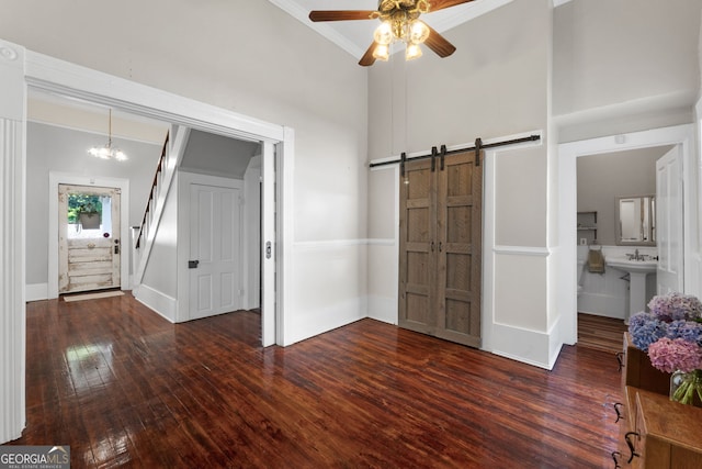 interior space featuring hardwood / wood-style floors, ensuite bath, a towering ceiling, a barn door, and ceiling fan with notable chandelier