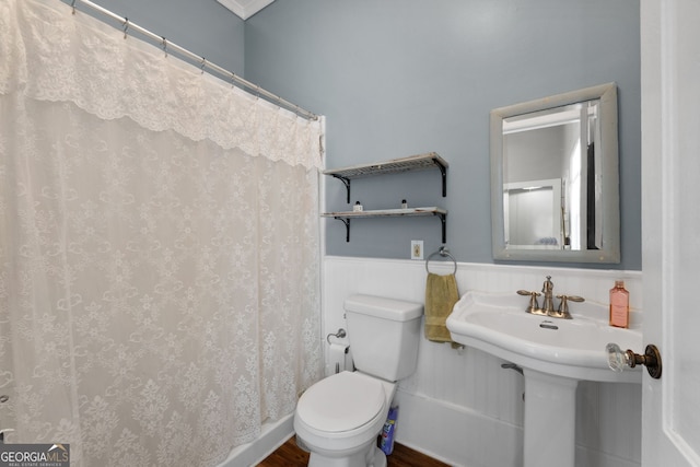 bathroom featuring a wainscoted wall, toilet, a shower with shower curtain, and wood finished floors