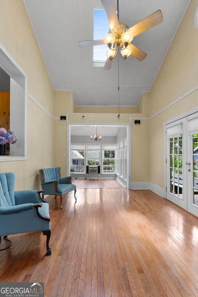 living room with ceiling fan with notable chandelier, baseboards, wood-type flooring, and high vaulted ceiling