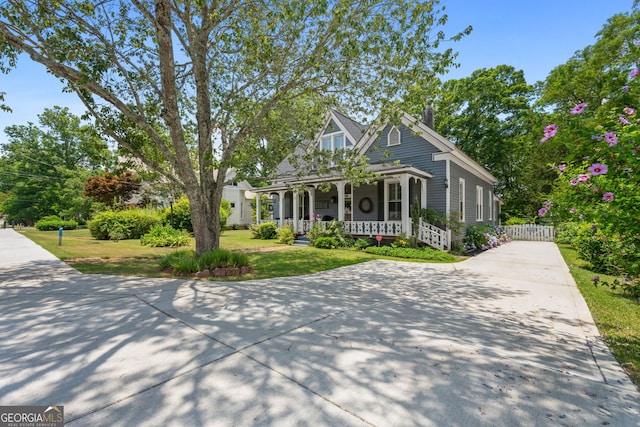 view of front facade with a porch, driveway, a front yard, and fence