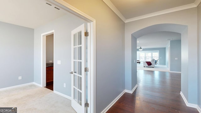 corridor with crown molding, dark wood-style floors, arched walkways, and baseboards