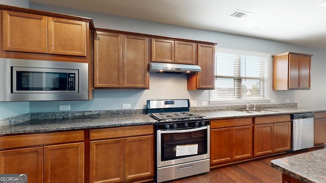 kitchen with under cabinet range hood, brown cabinets, dark wood-style floors, stainless steel appliances, and a sink