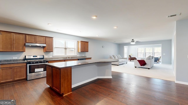 kitchen featuring gas stove, visible vents, under cabinet range hood, brown cabinets, and a center island