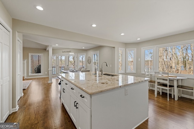 kitchen with light stone countertops, dark wood-style floors, white cabinetry, ornate columns, and a sink