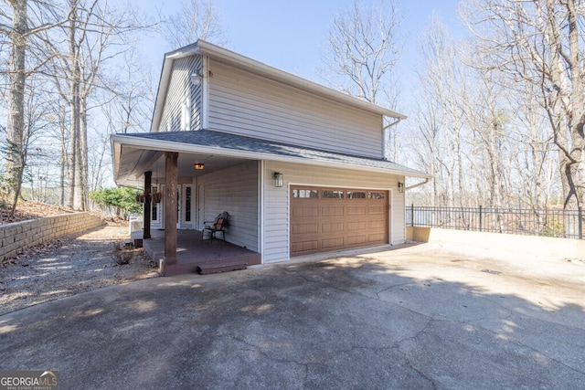 view of property exterior featuring a porch, an attached garage, fence, and driveway