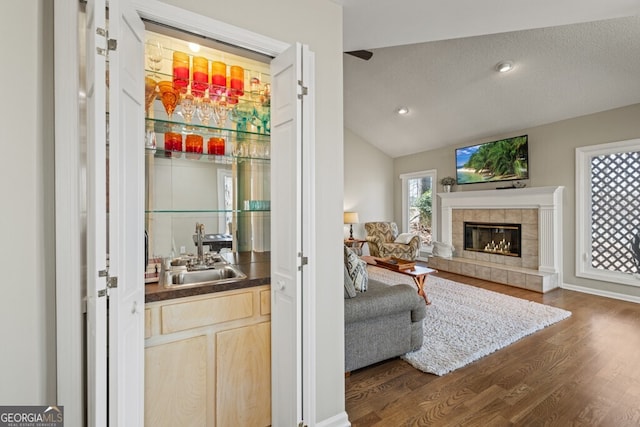 interior space featuring dark wood-style floors, a sink, indoor wet bar, vaulted ceiling, and a tiled fireplace