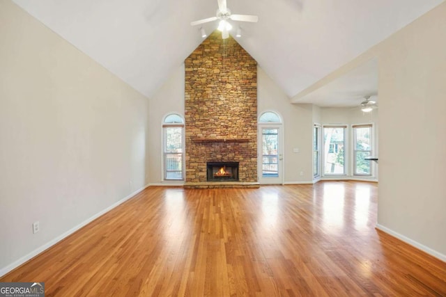 unfurnished living room featuring light wood finished floors, baseboards, a fireplace, high vaulted ceiling, and a ceiling fan