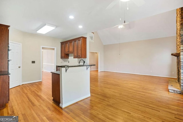 kitchen with a breakfast bar area, ceiling fan, decorative backsplash, dark countertops, and light wood-type flooring