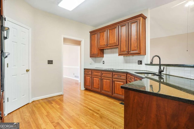 kitchen featuring dark stone counters, backsplash, light wood finished floors, and a sink