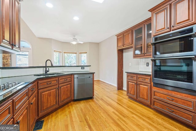 kitchen with a sink, decorative backsplash, light wood-style floors, stainless steel dishwasher, and double oven