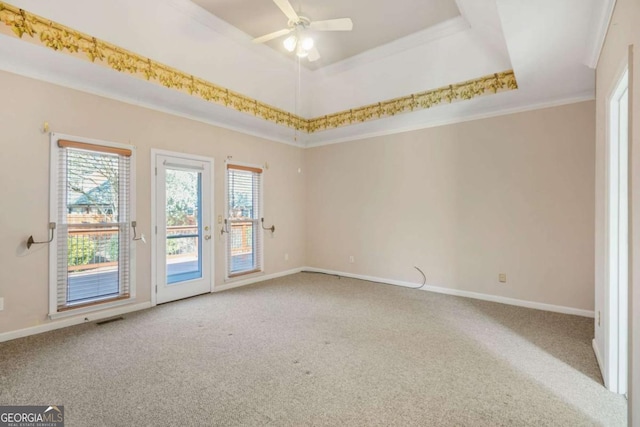 carpeted empty room with a ceiling fan, baseboards, visible vents, ornamental molding, and a raised ceiling