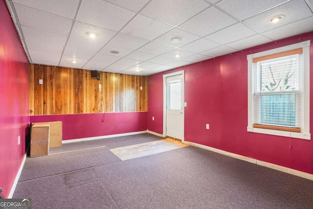 unfurnished room featuring a drop ceiling, baseboards, and wood walls