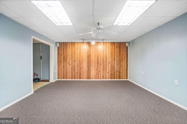 finished basement with ceiling fan, a drop ceiling, wood walls, and carpet floors