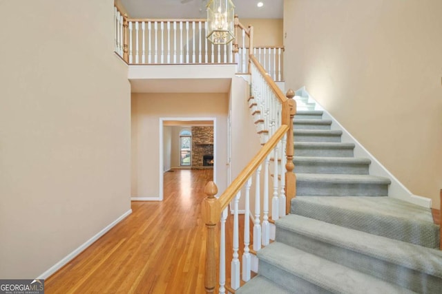 staircase with wood finished floors, baseboards, an inviting chandelier, a towering ceiling, and a large fireplace