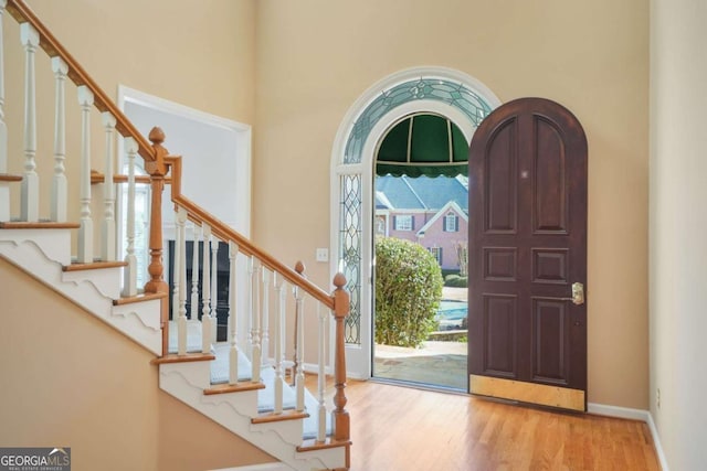 foyer entrance with stairway, baseboards, arched walkways, and wood finished floors